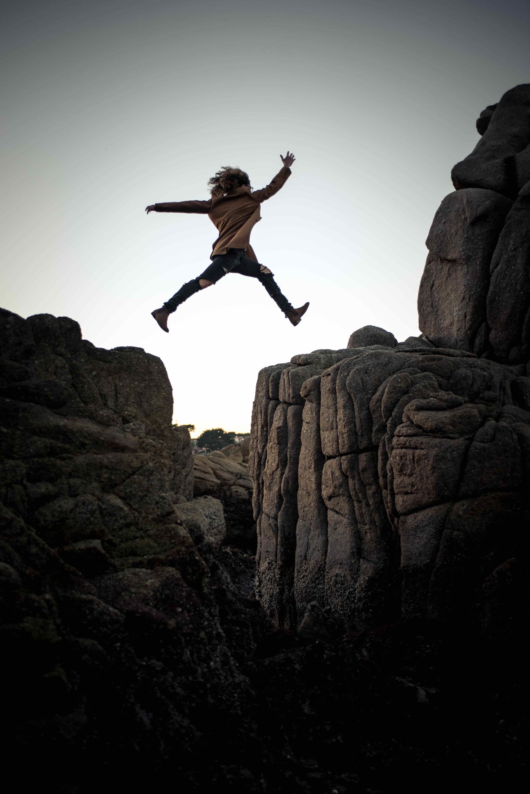 This image portrays a woman jumping across too big rocks to illustrate that she is fearless and courageous.