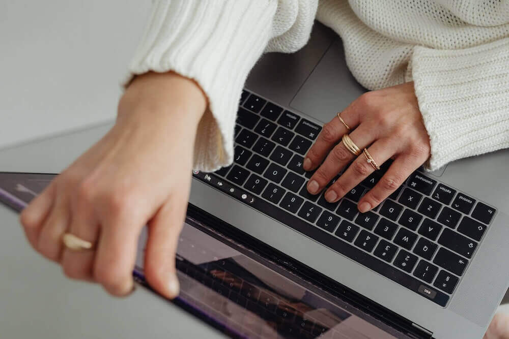 Woman in white sweater typing on a laptop